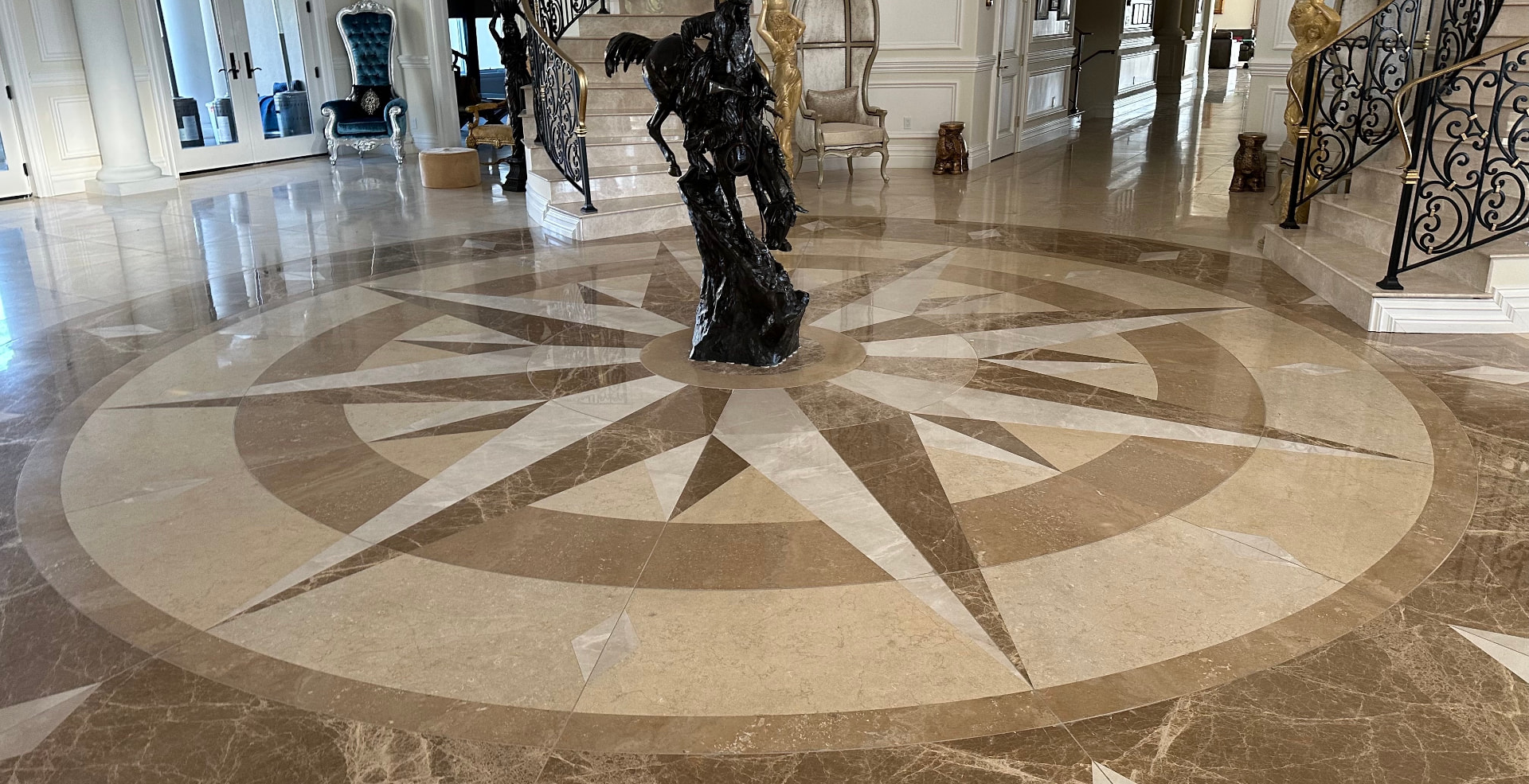 Intricate compass-star marble floor medallion in a grand foyer with a sweeping staircase