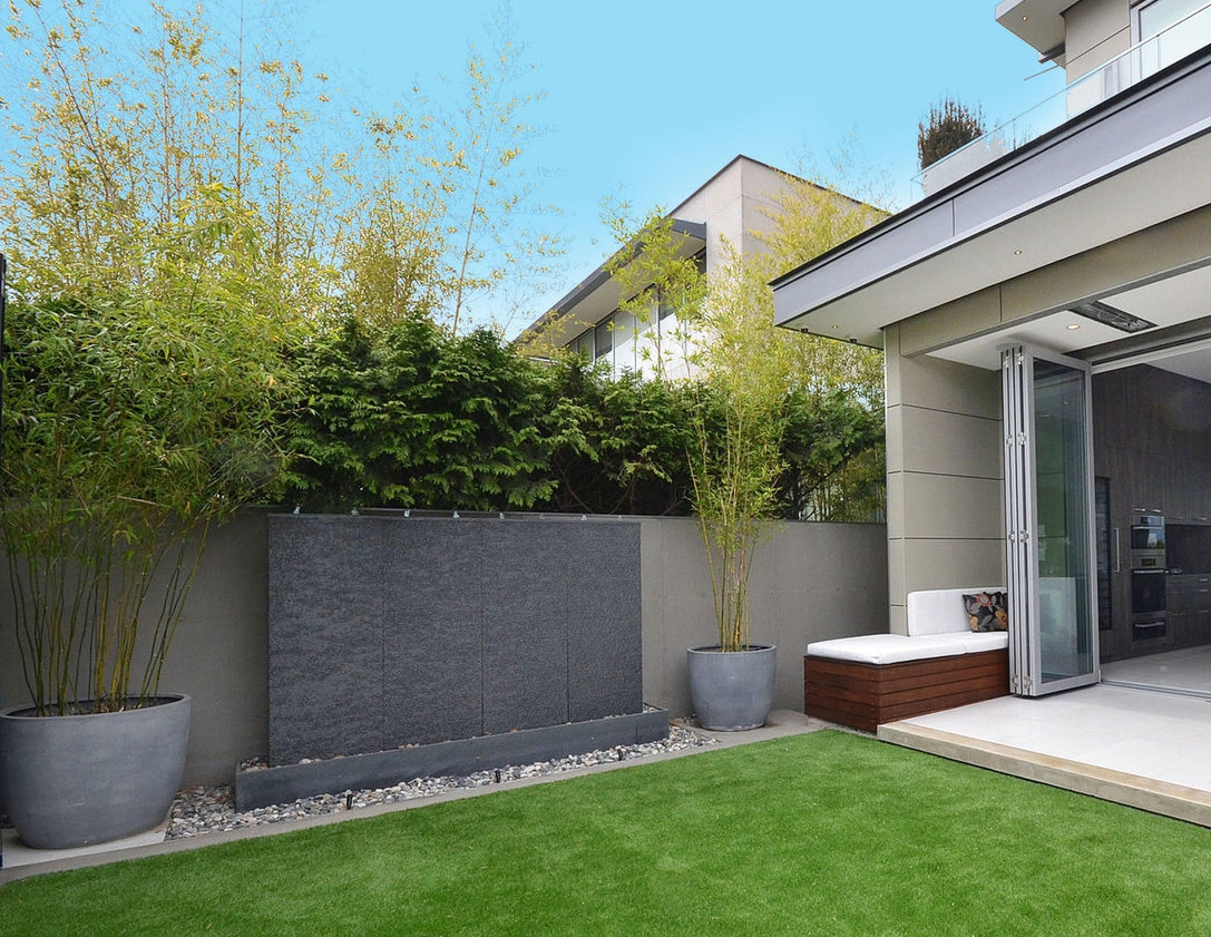 Dark granite water wall feature beside a bamboo-lined garden and modern home